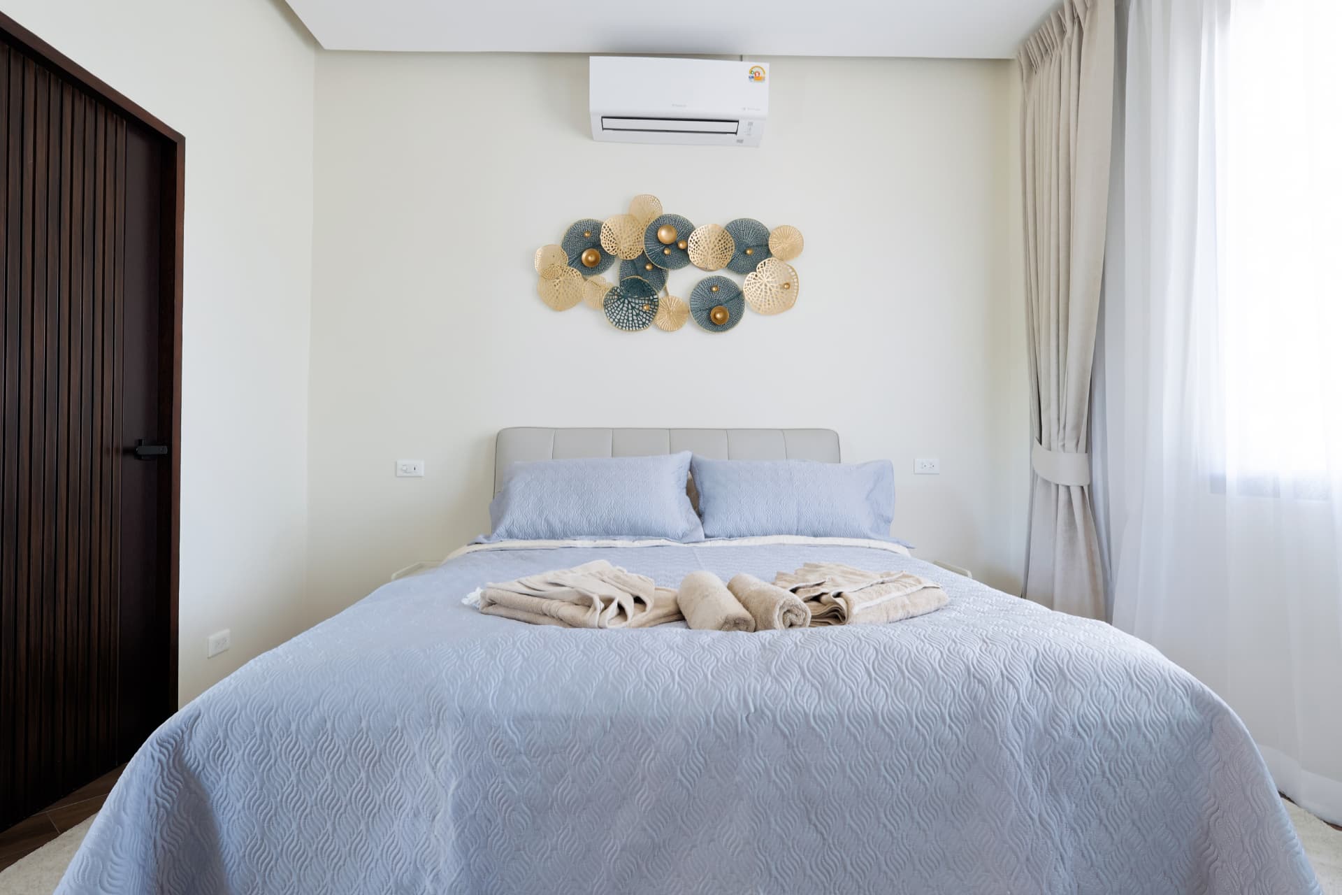 Bedroom with a double bed, folded towels, wardrobe and soft daylight through sheer curtains