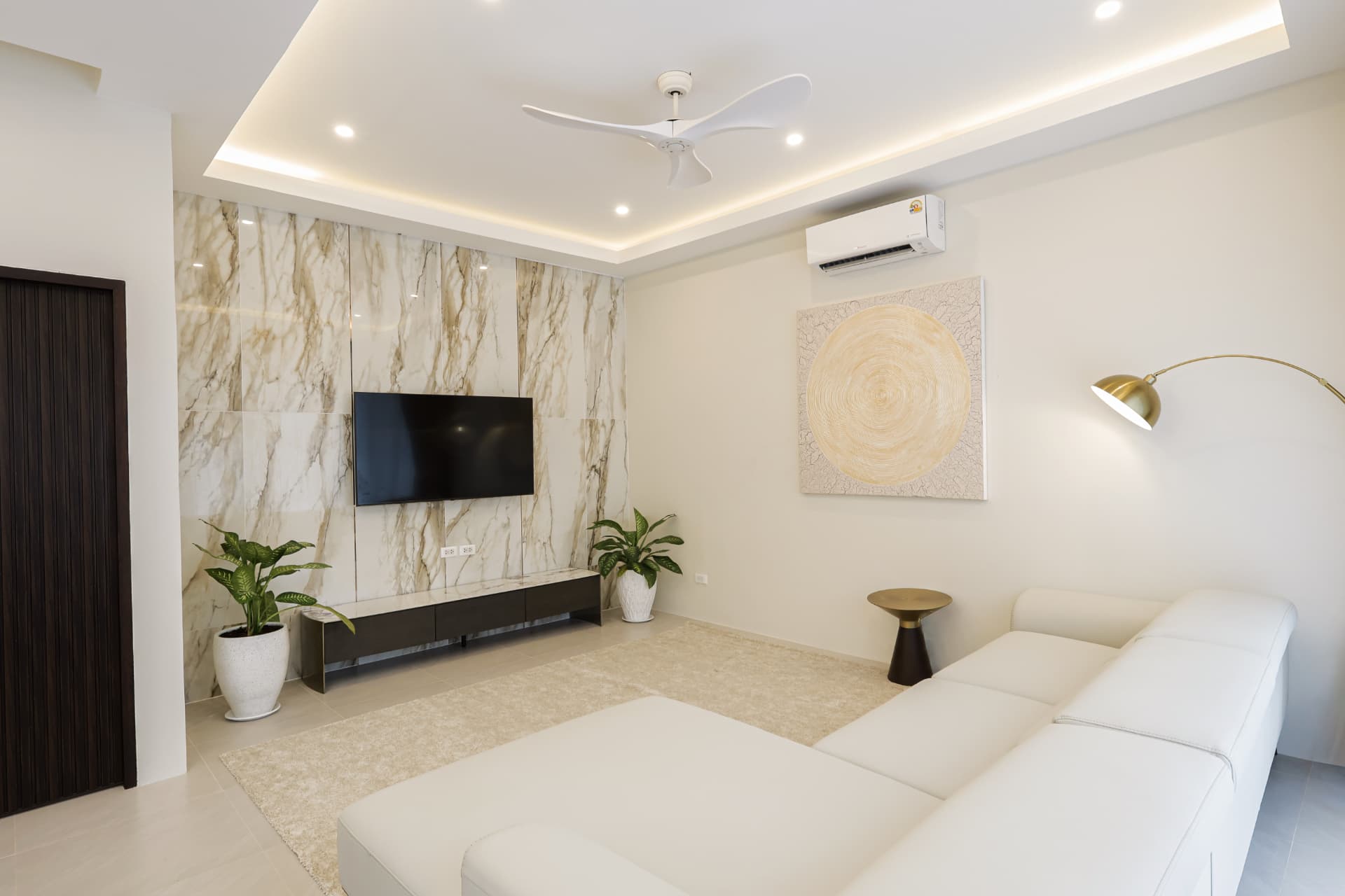Living room with a marble feature wall, wall-mounted television, cream sofa and brass floor lamp