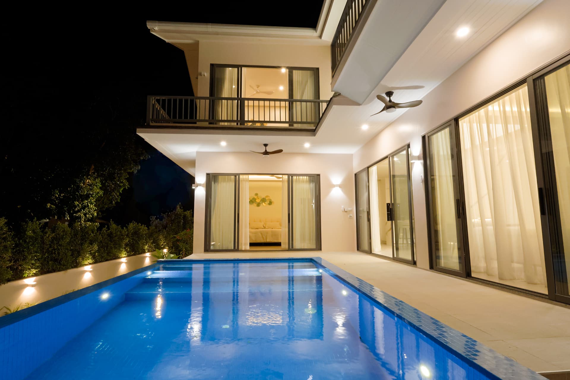 The long swimming pool at dusk running alongside the villa's lit terrace and sliding glass doors