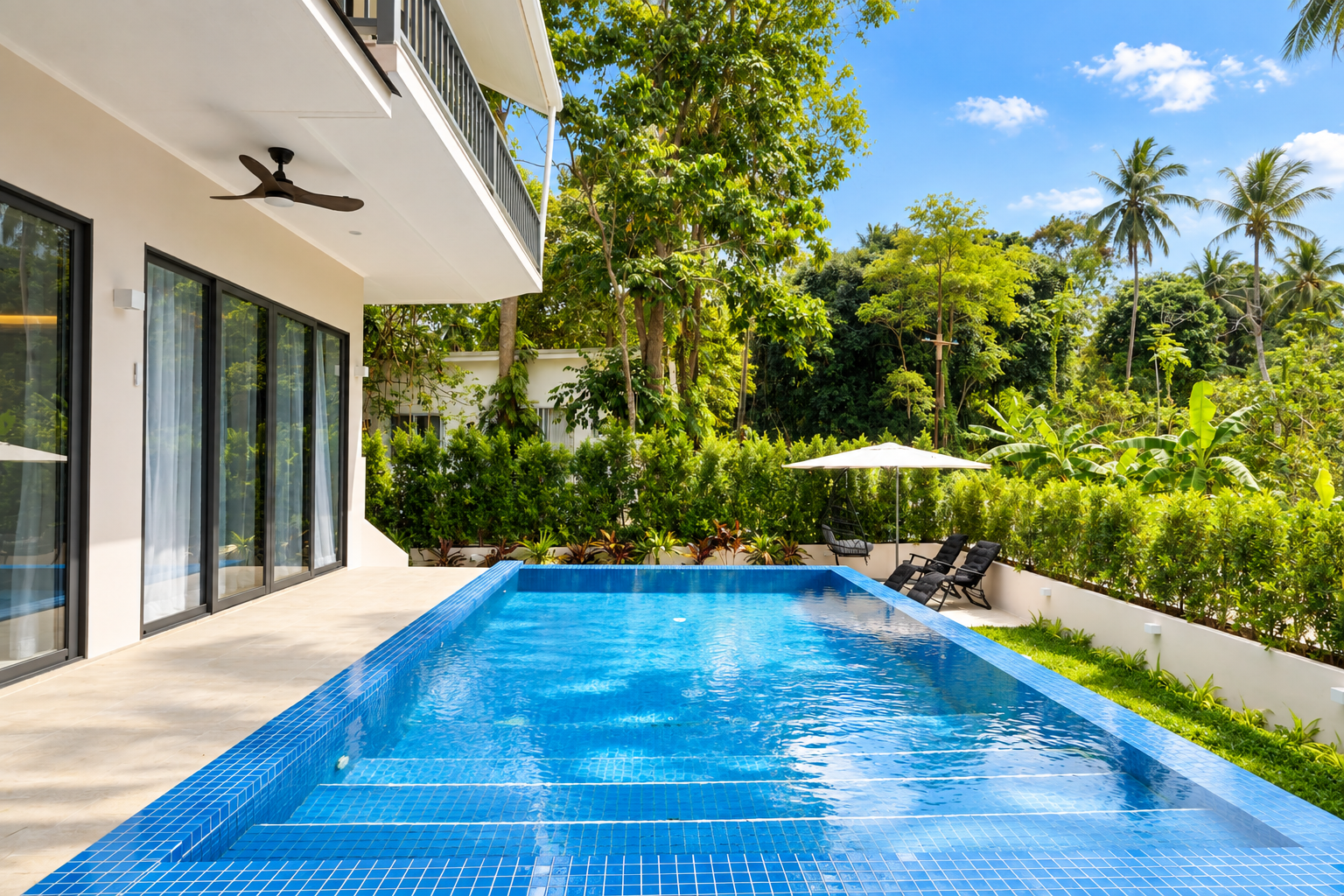 The swimming pool beside the terrace, with garden loungers, a parasol and jungle greenery behind