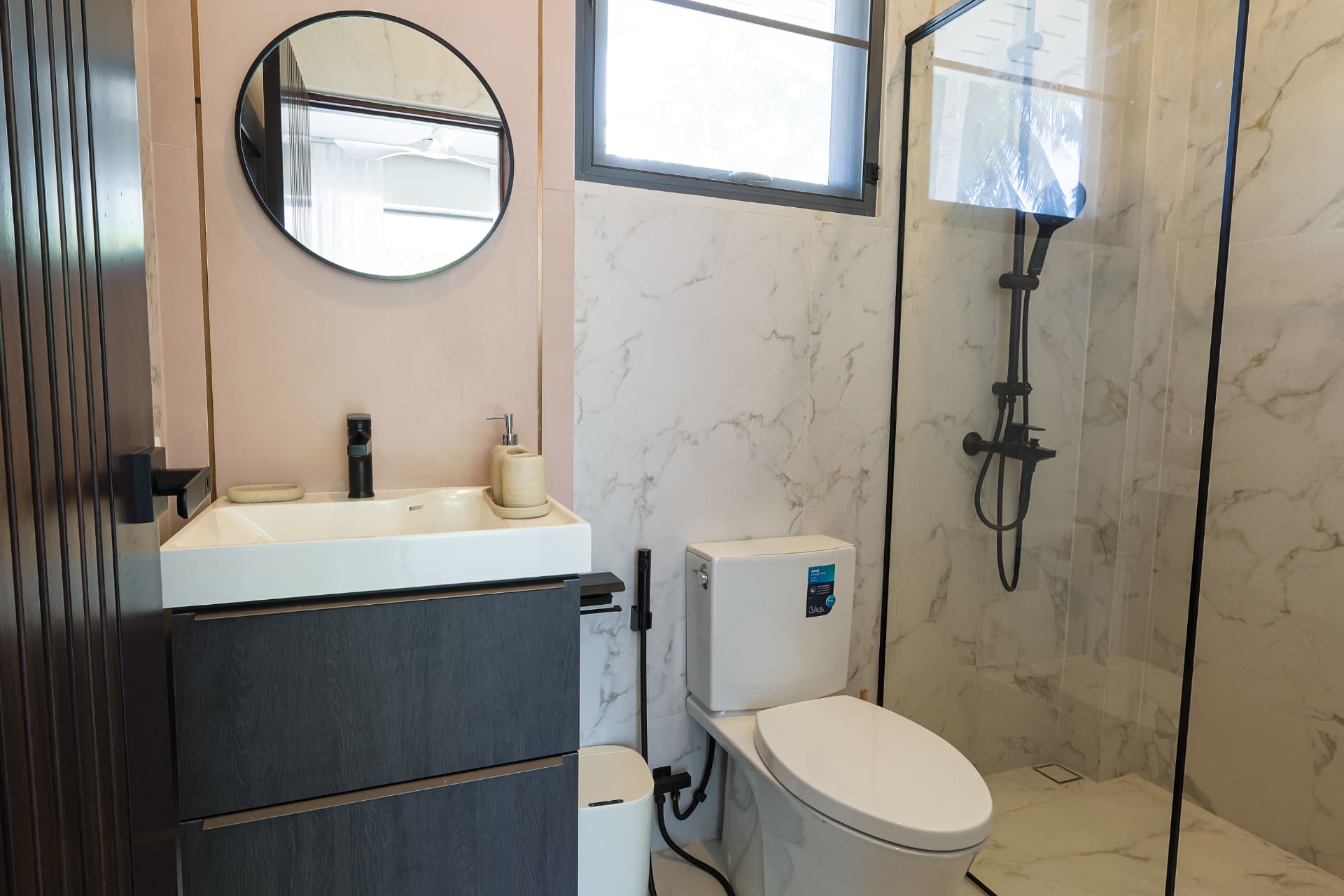 Second bathroom with a walk-in glass shower, washbasin with round mirror and marble tiling