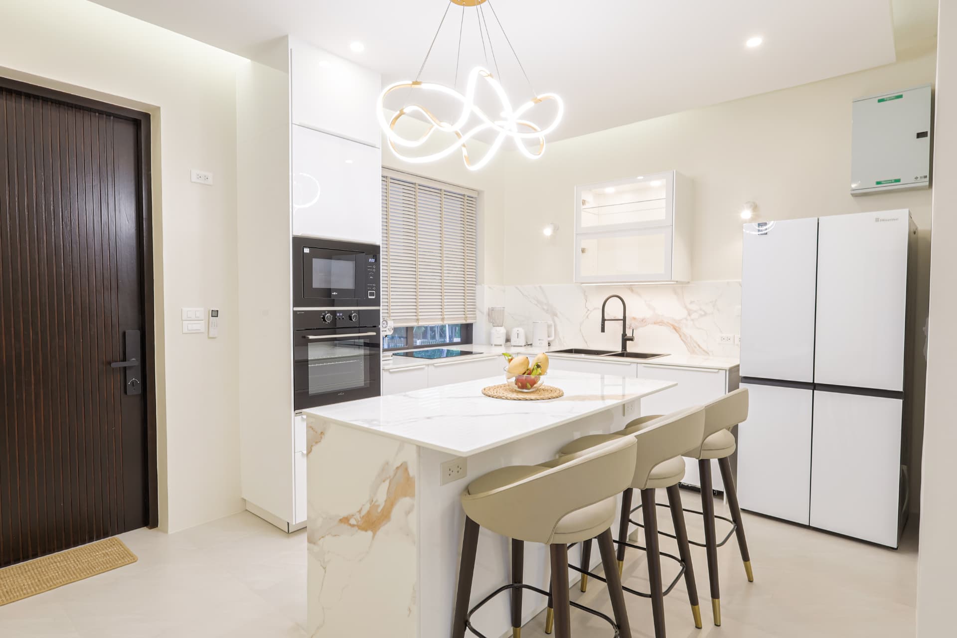White kitchen with marble island, bar stools, oven, microwave and large fridge