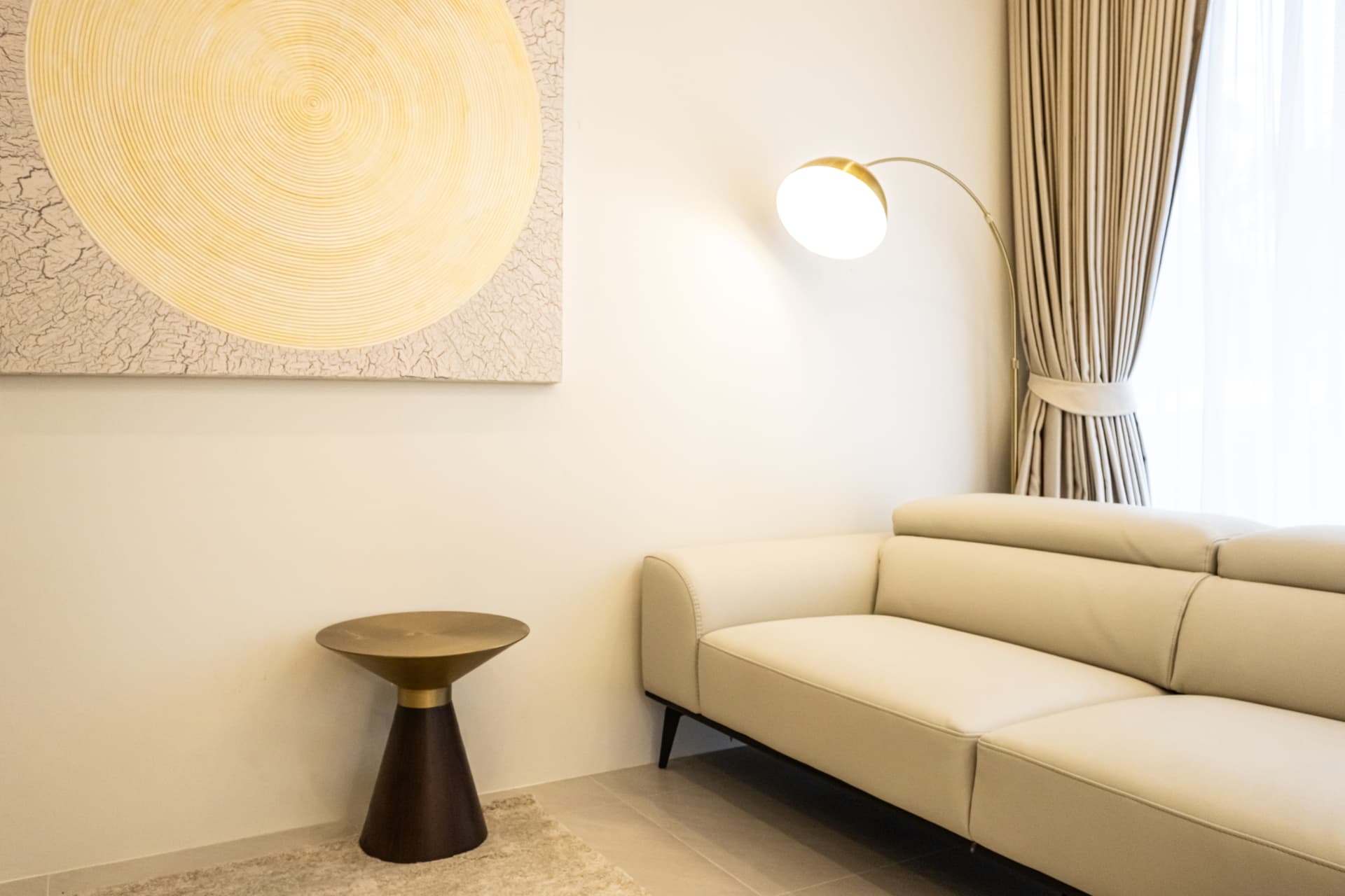 Corner of the living room with a textured sun artwork, brass side table and arc floor lamp